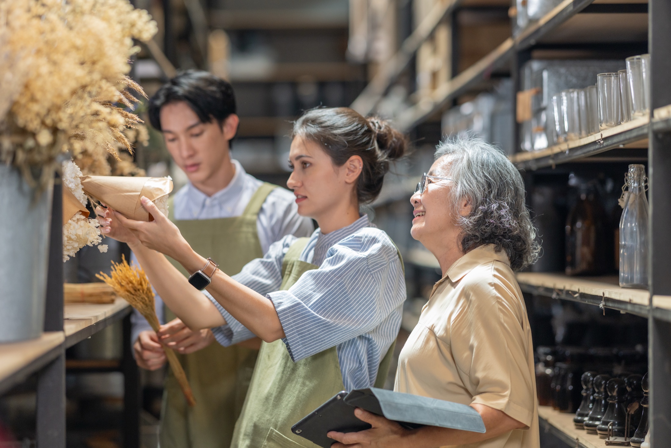 Three people examining products together on shelves in a small business storeroom.