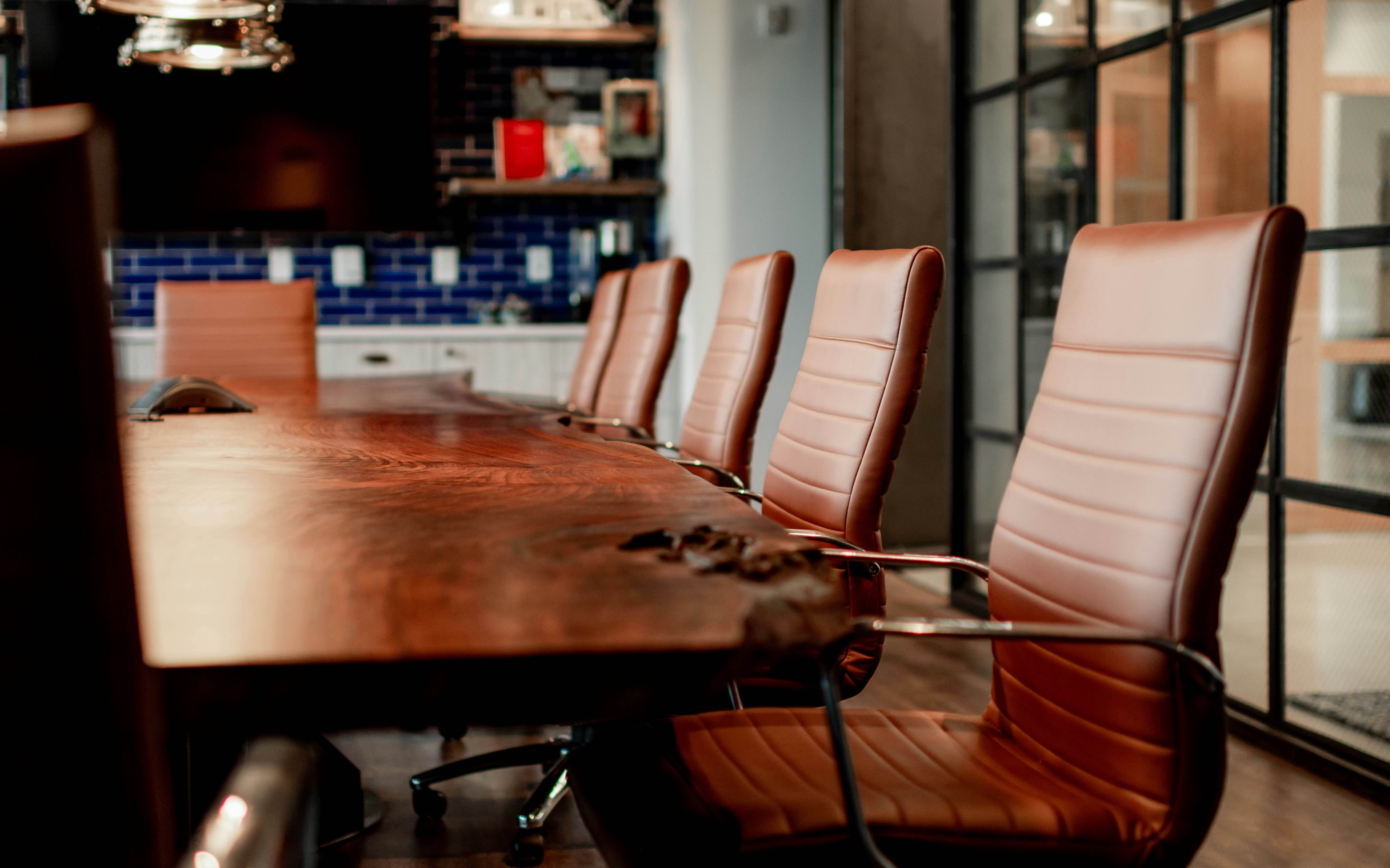 A long wooden boardroom table with leather chairs in a modern office.