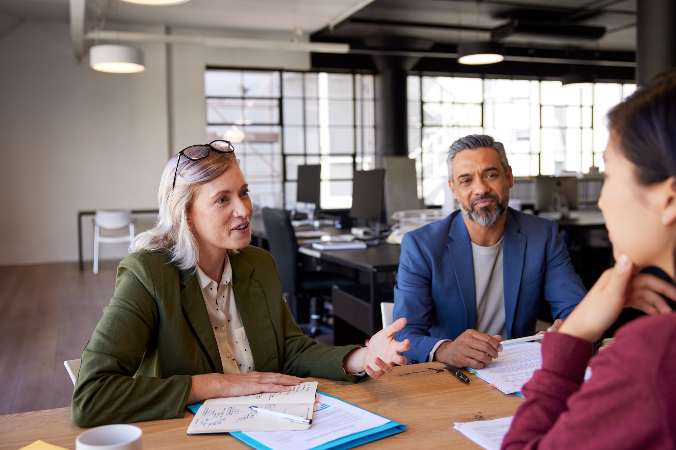 Three professionals discussing documents around a table in a bright modern office.
