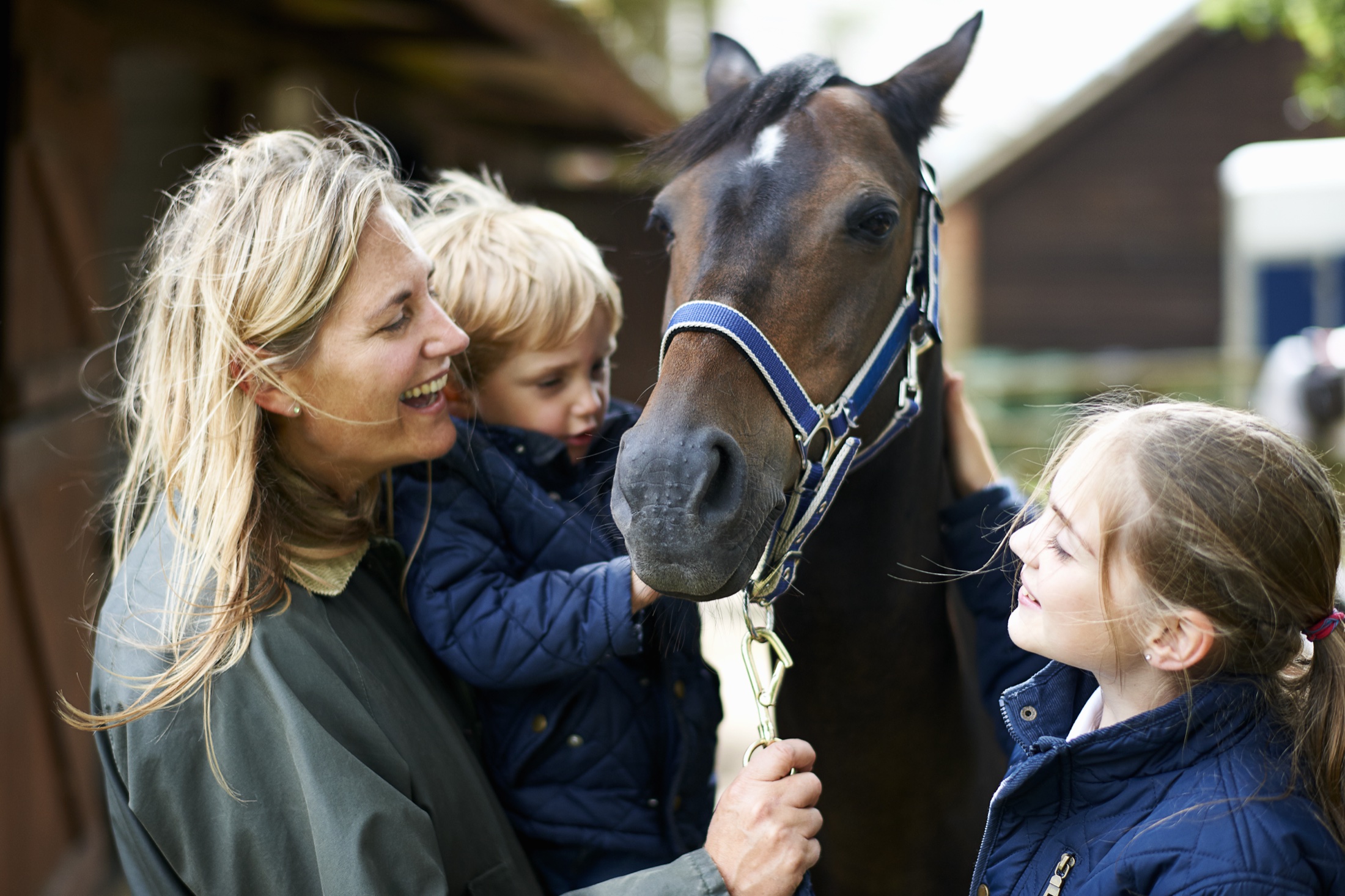 A mother and two children greeting a horse outside a stable.