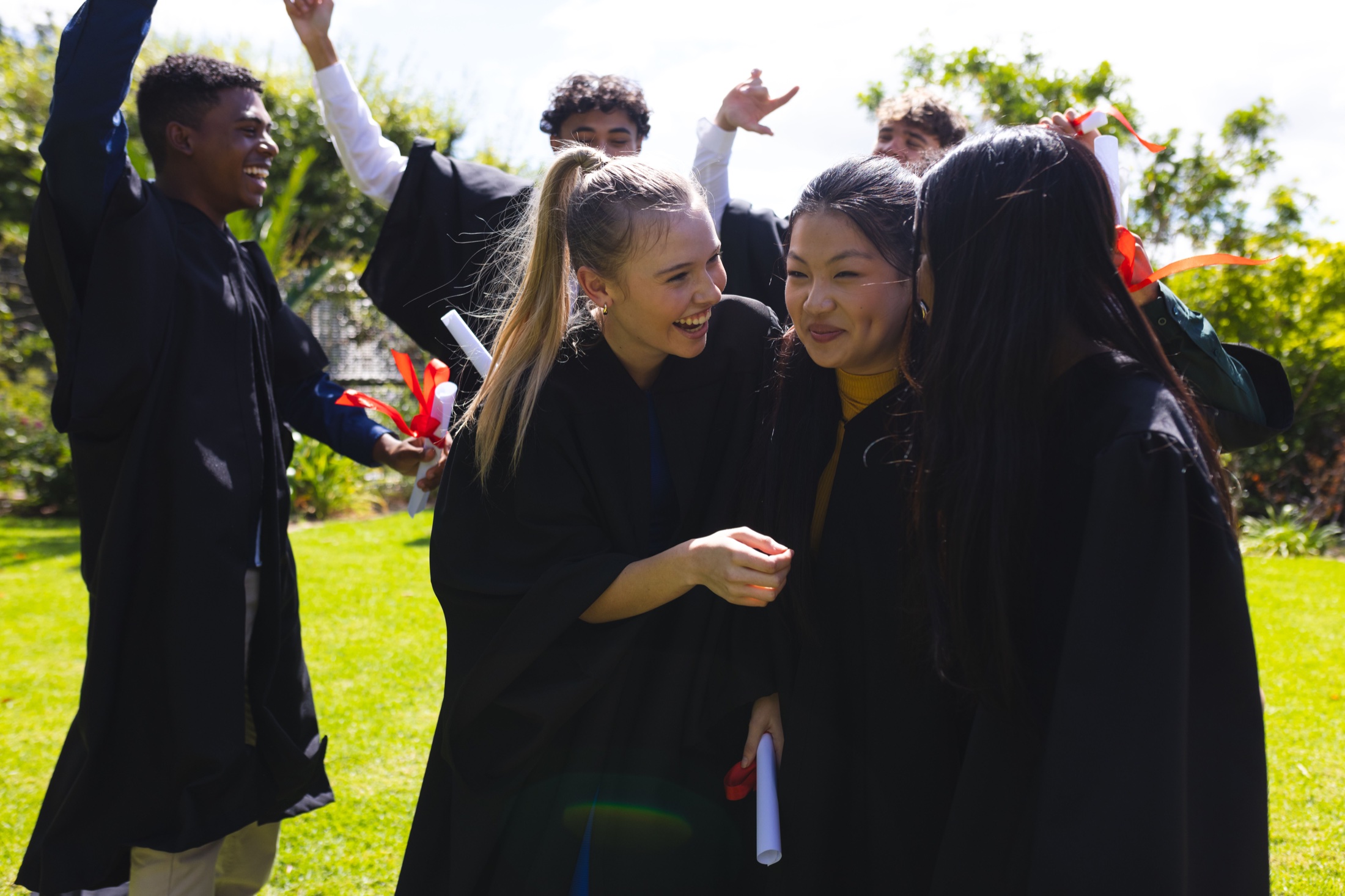 Graduates in gowns celebrating together outdoors, holding their diplomas.