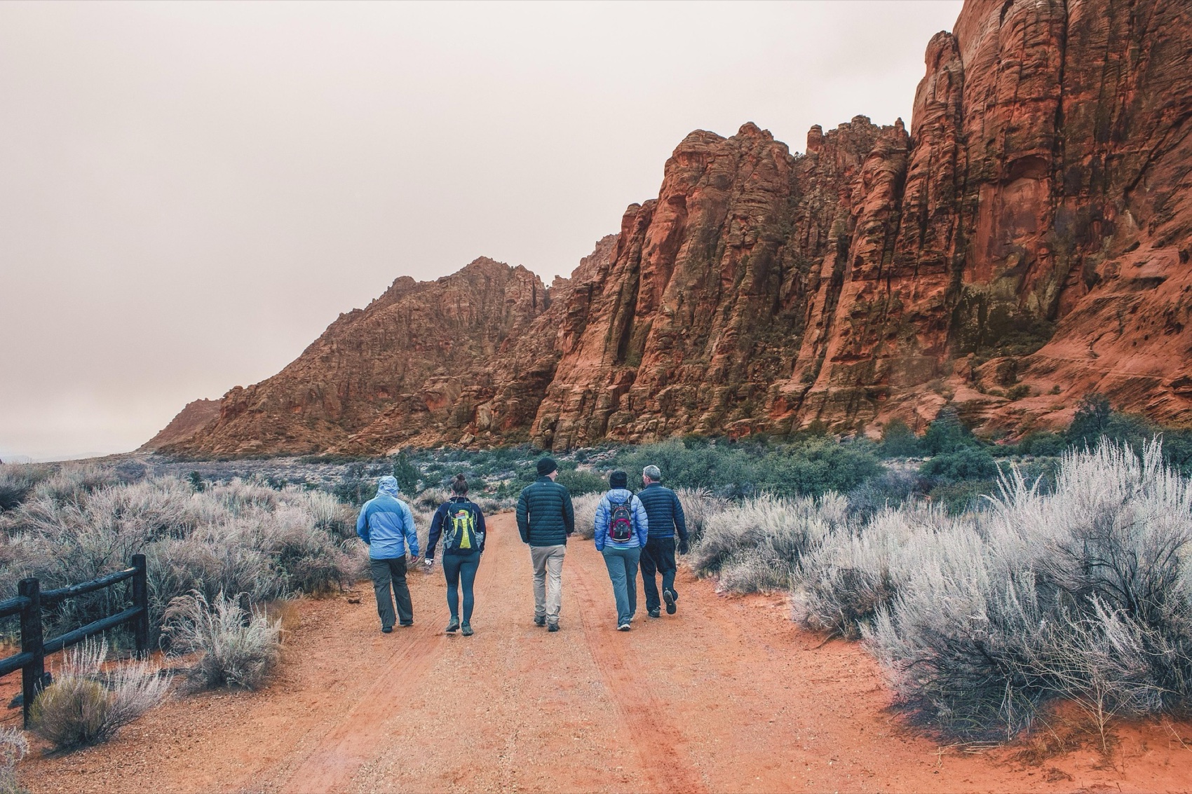 A small group walking together along a dirt path through a red-rock canyon landscape.