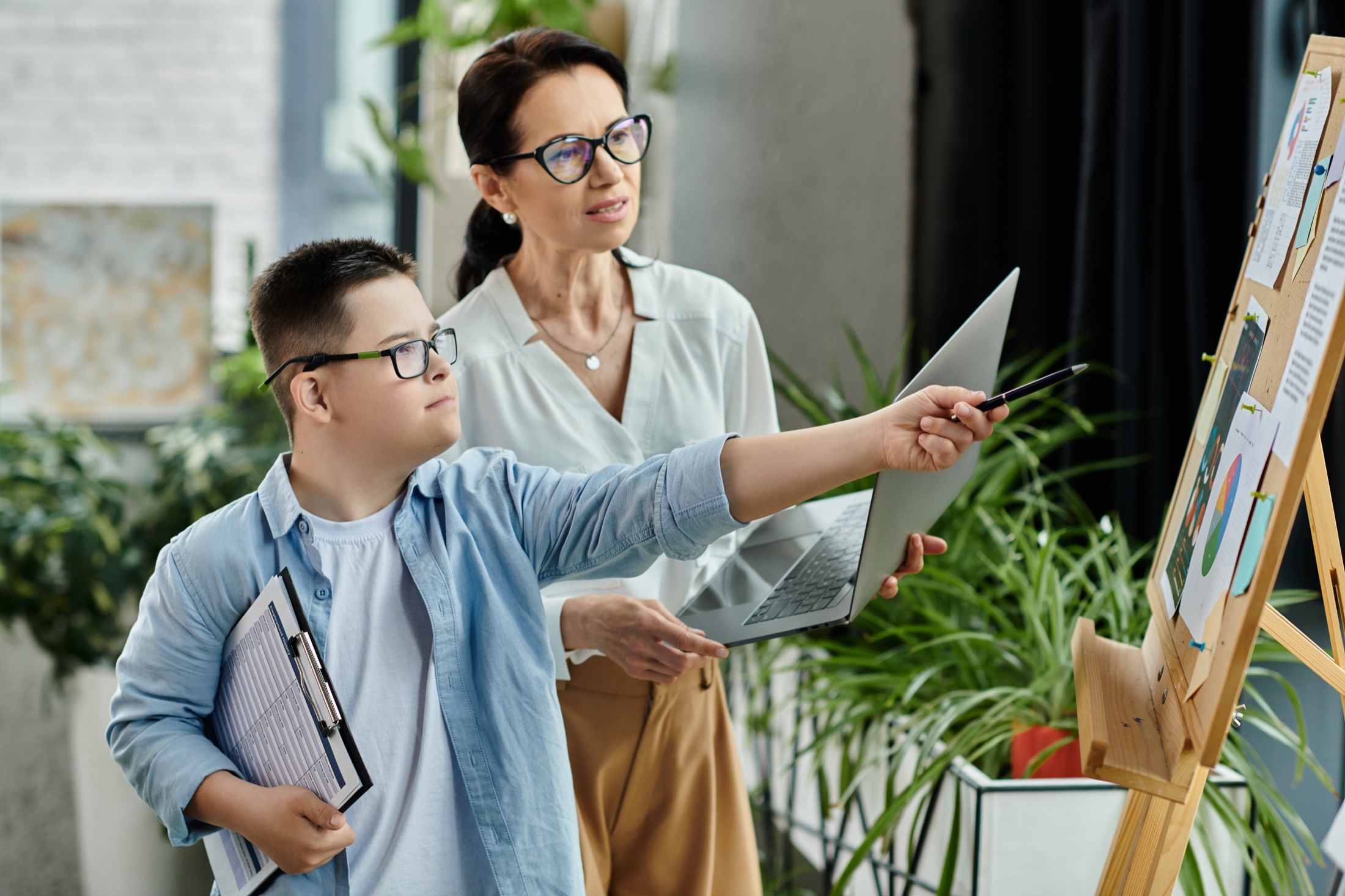 A woman and a boy looking at a project board together in an office, the boy pointing at it.