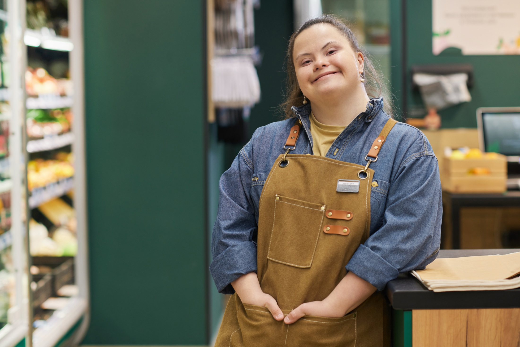 A young woman wearing an apron standing at the counter of a grocery store.