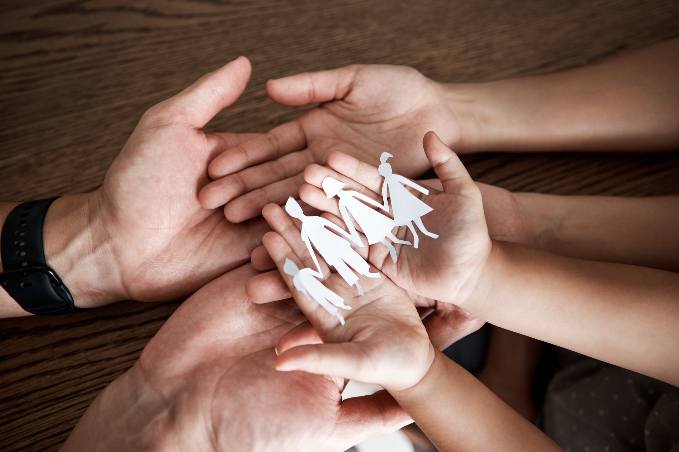 An adult's and a child's cupped hands holding a paper cutout of a family.