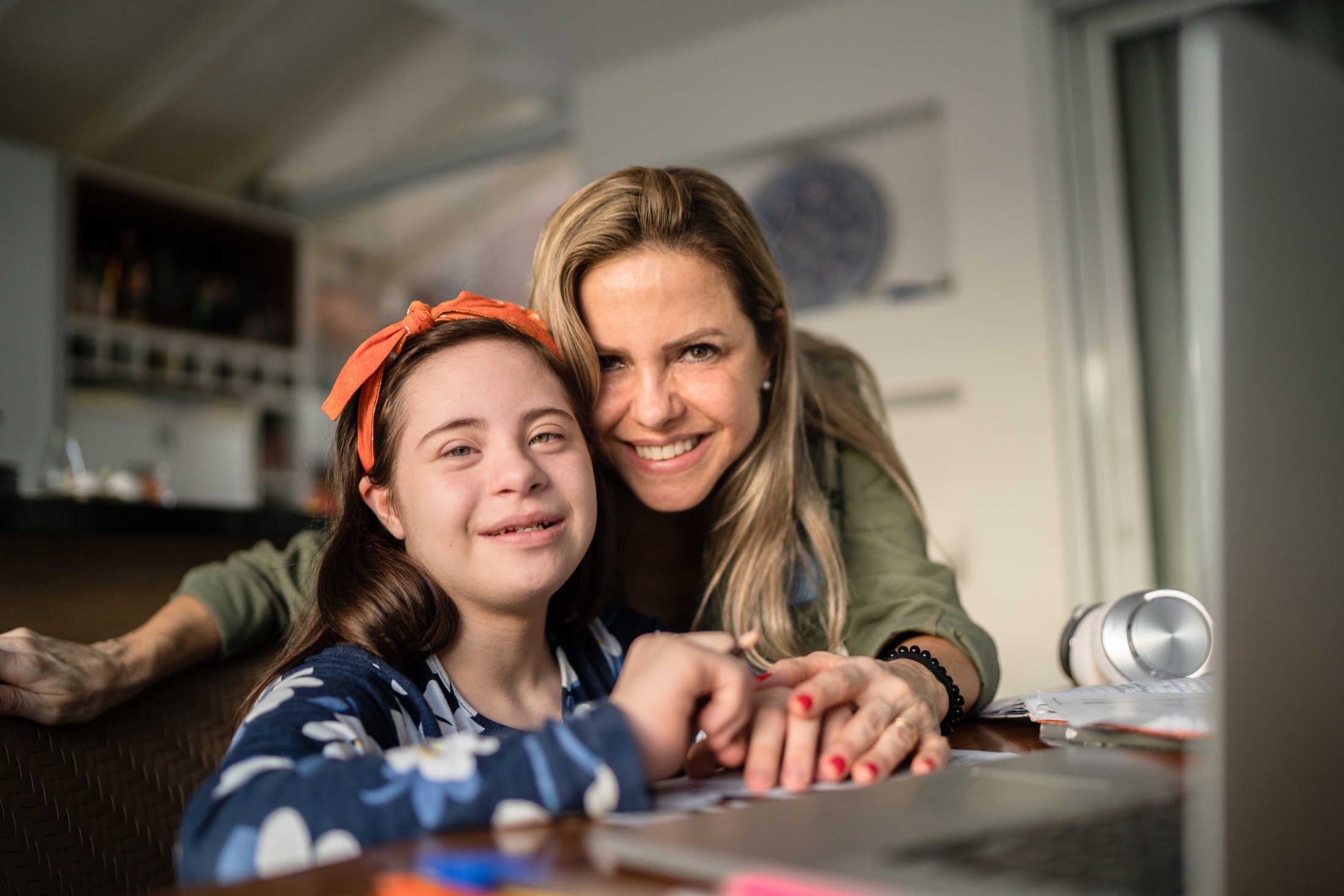 A mother and her daughter smiling together at a table at home.