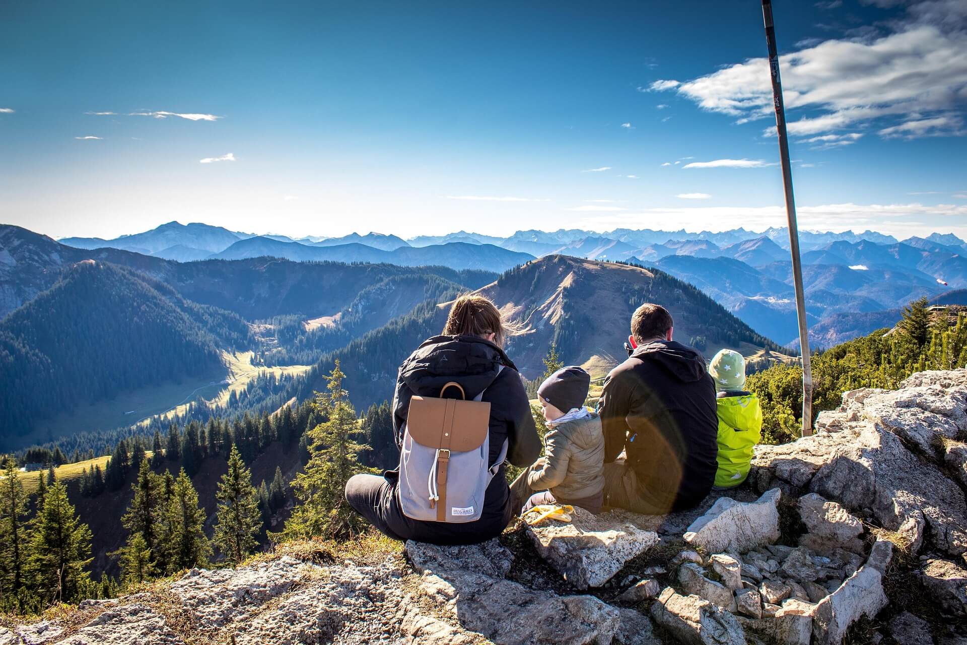 A family seated together on a mountain ridge, looking out over a wide valley.
